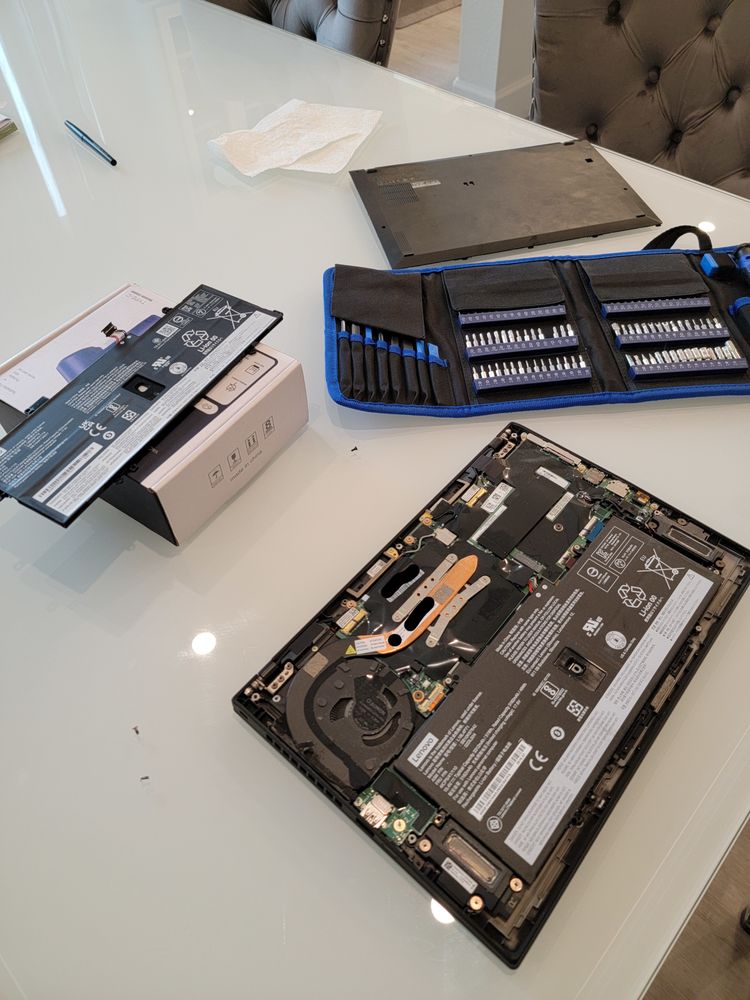 A laptop opened on a table during a battery and storage replacement, with a screwdriver kit laid out nearby.